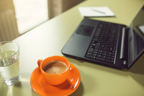 Laptop computer, cup of coffee, a note pad and a glass of water on the office desk