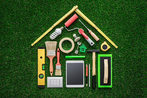 Home renovation, remodeling and DIY concept, work tools and tablet composing a house shape on the grass