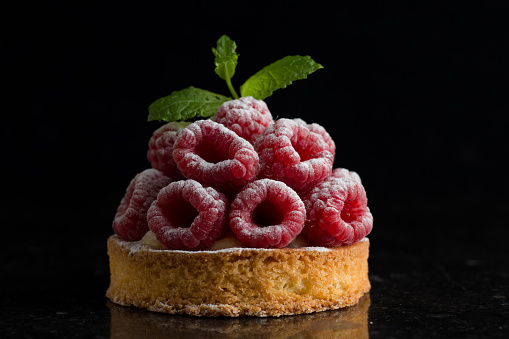 Raspberry cake dessert on dark background. Traditional french sweet pastry. Delicious, appetizing, homemade tart with custard, fresh berries and fruits. Copy space, closeup. Selective focus