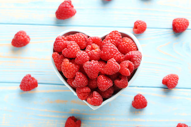 istock Red raspberries in bowl on a blue wooden table 586934736