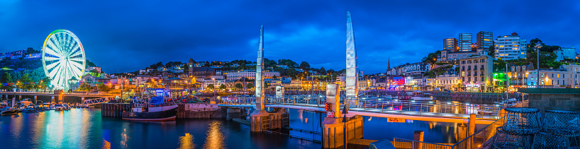 The hotels and villas, quayside shops, pubs and restaurants of Torquay overlooking the harbour illuminated at dusk.