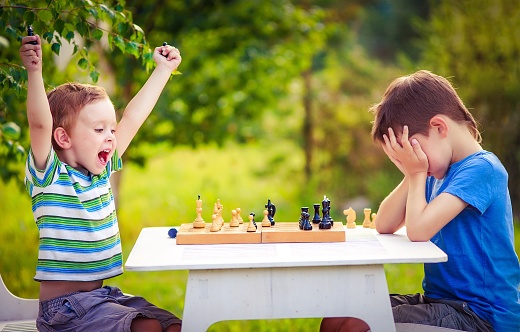 two young chess players outdoors. boy rejoices won a game of chess. sad opponent covered his face, and upset losing