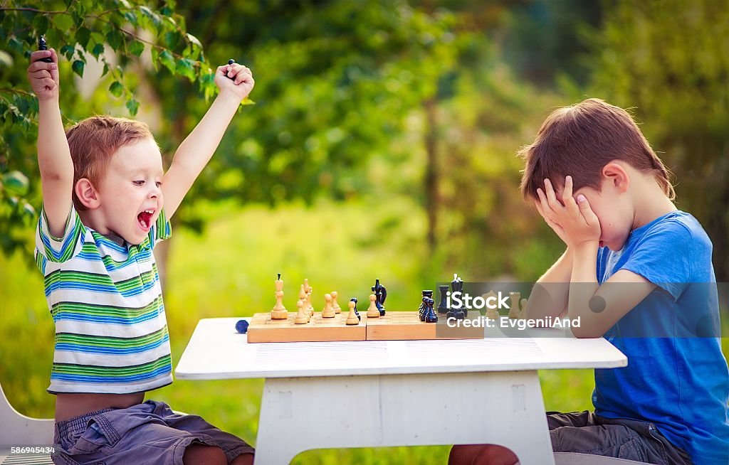 vivid emotions after the game of chess two young chess players outdoors. boy rejoices won a game of chess. sad opponent covered his face, and upset losing Child Stock Photo