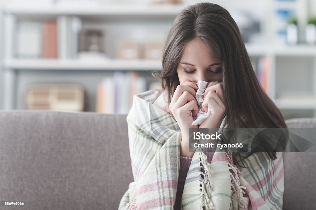 Sick woman with flu Sick young woman at home on the sofa with a cold, she is covering with a blanket and blowing her nose Cold And Flu Stock Photo