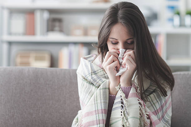 Sick woman with flu Sick young woman at home on the sofa with a cold, she is covering with a blanket and blowing her nose handkerchief photos stock pictures, royalty-free photos & images