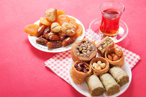 Turkish delight in a plate, glass cup of tea and dried fruit on red background. Eastern delight. baklava, burma baklava, Mebrume.