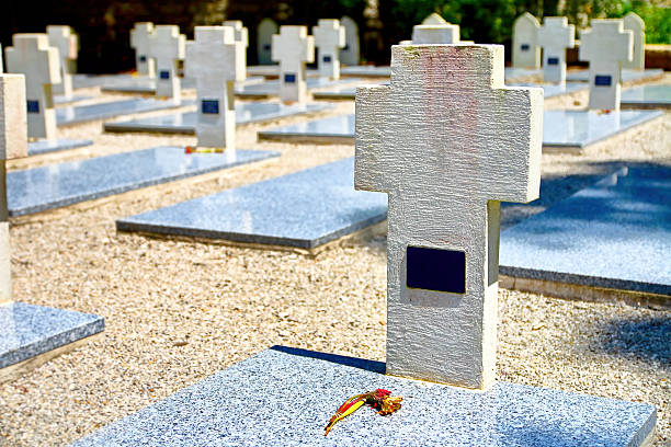 Horizontal composition color photography of white cross shape sculpture shapes in war memorial cemetery, memorial of maquis of Ain department and of resistance (Memorial des maquis de l'Ain et de la Resistance in french) during second World War (WWII) in small village of Cerdon in Ain, in Bugey mountains in Auvergne-Rhone-Alpes region in France (Europe). This monument of Resistance of Ain and Haut Jura, also named the Valley of Hell (memorial du Val d'Enfer in french), is a memorial attended a memorial and cemetery. This War Memorial, dedicated to the memory of 700 dead maquis of Ain and Haut Jura, will remain a testimony of gratitude to those who gave their lives for our freedom. This cemetery brings 89 graves of resistance fighters or victims of the Shoah; it was inaugurated June 24, 1956 by General de Gaulle. Among them, in addition to local maquis leaders, there are those of foreigners who came to fight in the Ain. Spaniards, Poles, Italians, North Africans lie to their fellow soldiers. Each May 8 ceremony honors all those guerrillas fell for the liberation of France. Shot with a dried flower on granite and marble tomb stone. Names are not recognizable on gravestones or have been removed, and it's a public place.