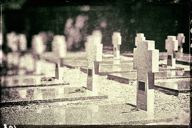 Horizontal composition sepia toned color photography of cross shape sculpture shapes in war memorial cemetery. Shot with dried flowers on granite and marble tomb, gravestones. This picture was is retro styled with some vignette and cracked border. Names are not recognizable on gravestones or have been removed, and it's a public place.