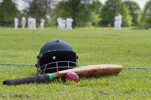 Cricket helmet, bat and ball on boundary line during a game in the English village. 