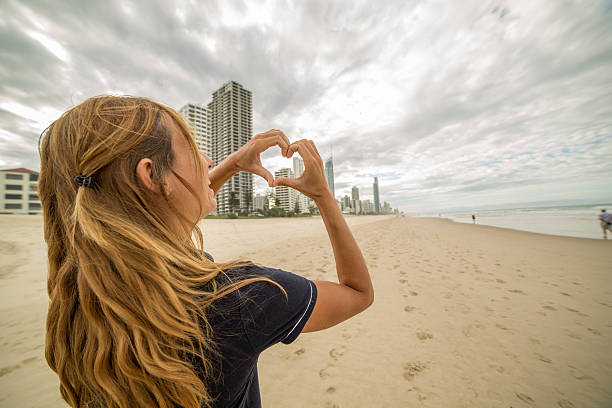 istock Young woman frames Surfer's paradise beach into heart shape 587196250