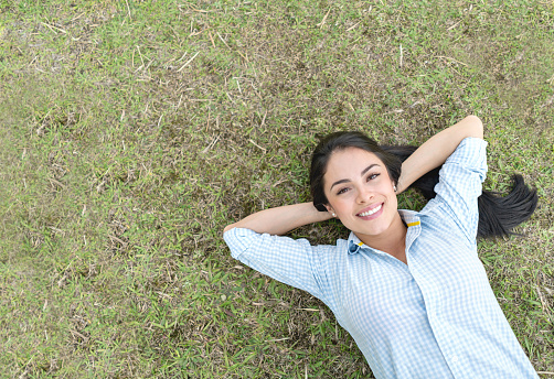 Beautiful Latin American woman relaxing at the park lying on the floor and looking very happy