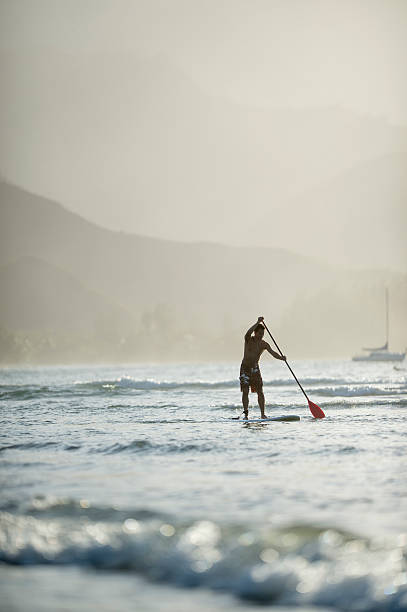 SUP in Hawaii A young adult man is paddle boarding while on vacation in Hawaii. north shore stock pictures, royalty-free photos & images