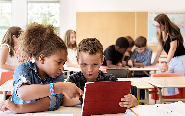 school kids in class using a digital tablet - klaslokaal fotos stockfoto's en -beelden