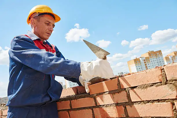 construction worker. mason bricklayer installing red brick with trowel putty knife outdoors