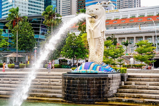 May 2020. Singapore. Several people seen in the shot taking picture near the famous monument in Merlion Park Singapore landmark and a major tourist attraction, located near One Fullerton, Singapore, near the Central Business District. The Merlion is a mythical creature with a lion's head and the body of a fish that is widely used as a mascot and national personification of Singapore. Some people are seen wearing masks while others don't wear masks during the COVID 19 / Coronavirus pandemic.