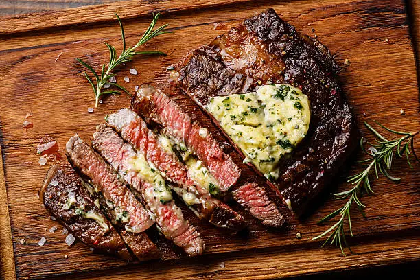 Sliced grilled Medium rare barbecue steak Ribeye with herb butter on cutting board close up