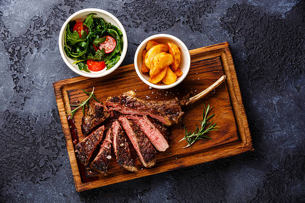 Sliced grilled Veal rib with potato wedges and salad Sliced grilled Medium rare barbecue Steak on bone Veal rib with potato wedges and salad with tomatoes and arugula on dark background steak salad stock pictures, royalty-free photos & images