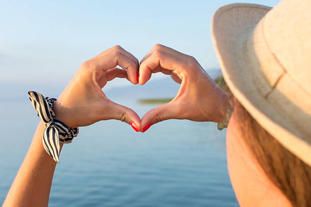 istock Woman hands making heart shape at the beach 587209124