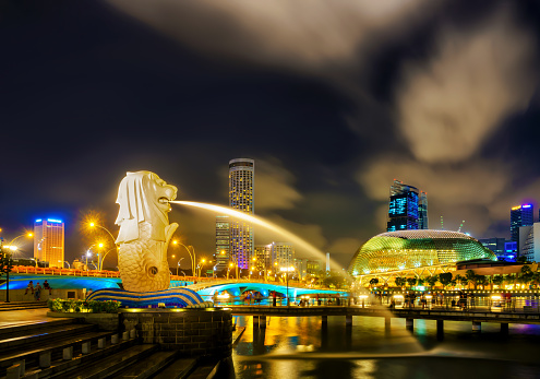 Singapore, Singapore - March 1, 2016: Merlion statue spraying the water from its mouth at Merlion Park in Downtown Core of Singapore at Marina Bay at night. Skyscrapers and Esplanade on background