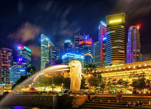 Singapore, Singapore - March 1, 2016: Merlion statue spraying the water from mouth at Merlion Park in Downtown Core of Singapore at Marina Bay at night. Skyline with Skyscrapers on background