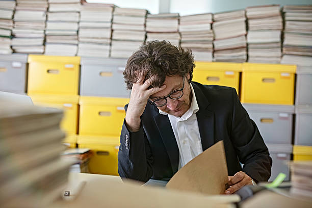 istock Frustrated businessman sitting at desk Overloaded With Paperwork 587210428