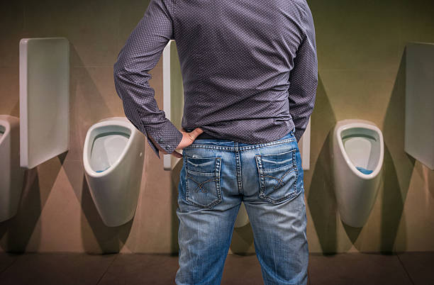 Standing man peeing to a urinal in restroom stock photo