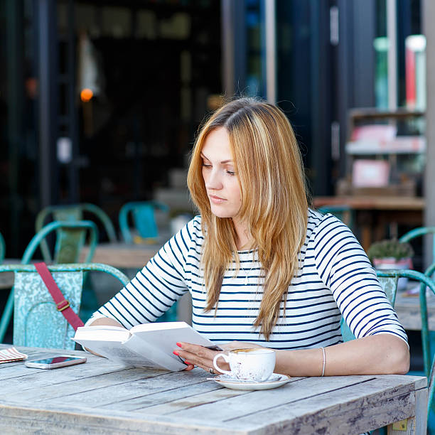 istock Woman drinking coffee and reading book in cafe 587228624