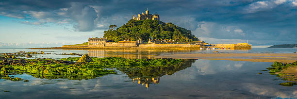 Cornwall St Michaels Mount ocean island summer sunrise panorama UK Warm summer sunlight illuminating the historic chapel, hamlet and harbour of St. Michael's Mount, reflecting in the tranquil waters of Marazion, Cornwall, UK.Warm summer sunlight illuminating the historic chapel, hamlet and harbour of St. Michael's Mount, reflecting in the tranquil waters of Marazion, Cornwall, UK. marazion photos stock pictures, royalty-free photos & images