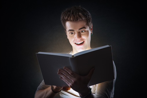 Young smiling man reading an exciting book glowing in the dark