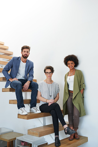 Portrait of three young creatives alongside a staircase in a modern office