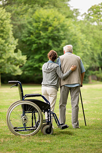 senior man with caregiver at the park - wheelchair disabled senior adult female nurse imagens e fotografias de stock