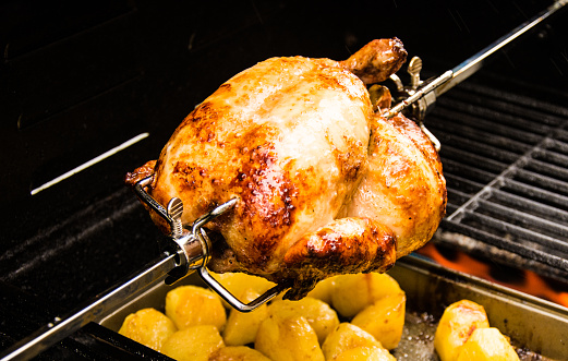 Cooking chicken on a barbecue rotisserie is an ideal way to achieve suculent, tasty chicken. The image here shows a chicken being cooked with potatoes in a tray cooking below it.