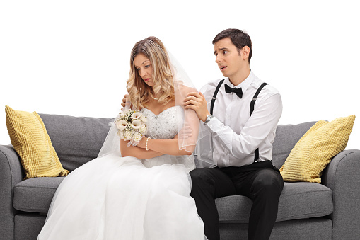 Young groom trying to appease his angry bride isolated on white background