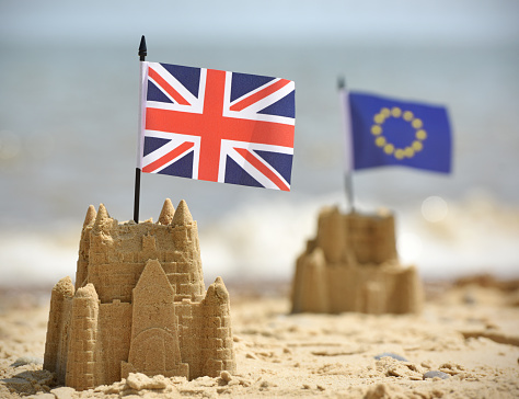 Two sandcastles on a British beach with UK and European Union flags. the point of focus is the UK Union Jack.