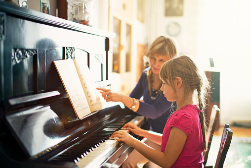 A young girl is playing the piano. She is wearing a blue shirt and a red bow. The piano is white and has black keys