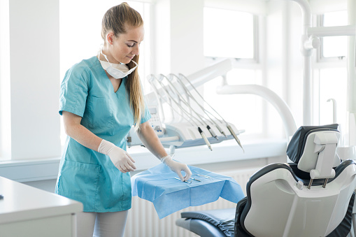 Smiling dentist arranging dental equipment. Professional is wearing scrub. She is standing by chair in clinic.