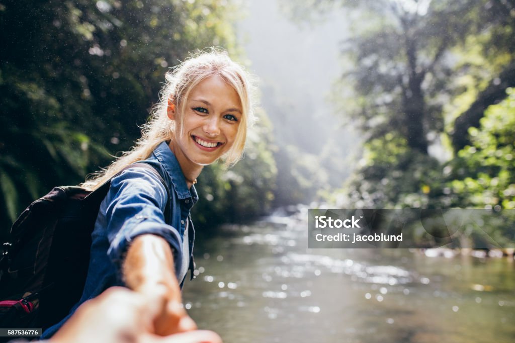 Female hiker holding hand of his boyfriend Portrait of happy young woman holding hand of her boyfriend while walking by mountain stream. Couple enjoying a hike in nature. Women Stock Photo