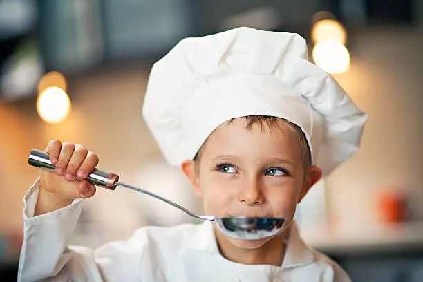 Photo of Little boy chef tasting soup.