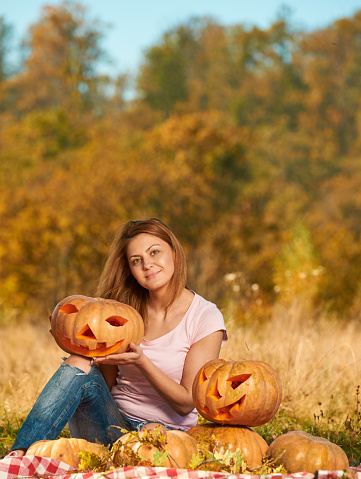 happy young woman in autumn day in nature holding Halloween pumpkin and smiling at camera.
