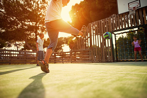 Kids playing football in the schoolyard Little boys and a girl playing football in the schoolyard. The boy aged 6 is shooting the football at the goal. Little girl is a goalkeeper. Sunny summer evening. recess soccer stock pictures, royalty-free photos & images