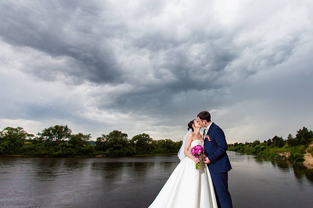 The bridegroom is kissing the bride on the river bank stock photo