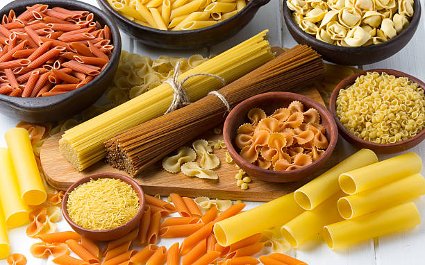 diversi tipi di pasta sul tavolo in legno bianco. sfondo - pasta whole wheat spaghetti raw foto e immagini stock