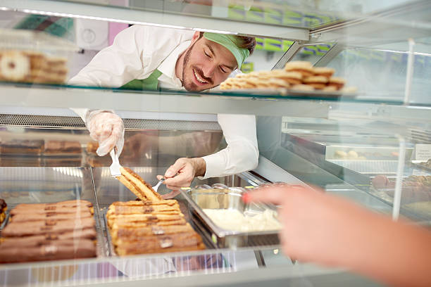 istock Vendor in bakery taking out biscuit with cream from showcase 587549910