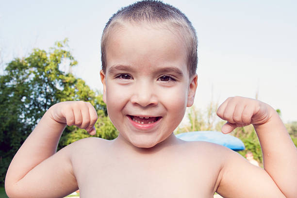 маленький беззубый мальчик, сгибающий мышцы - flexing muscles little boys human muscle strength стоковые фото и изображения