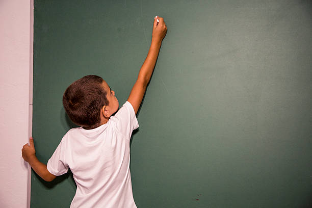 istock Boy standing in front of school blackboard or chalkboard. 587778896