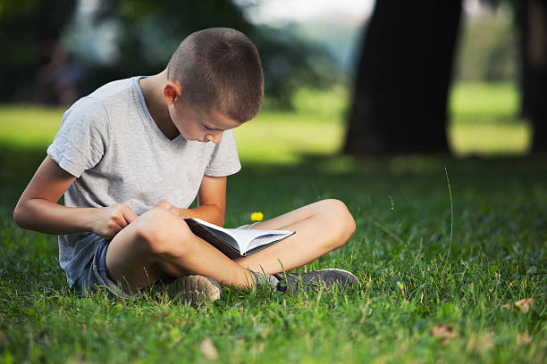 istock Cute boy sitting in nature and reading a book 587779732
