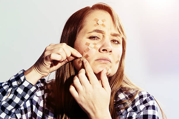 istock Frowning woman adding adhesive bandage to many others on face 587797748
