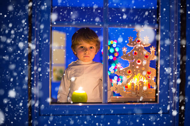 istock Little kid boy standing by window at Christmas with snow 587810108