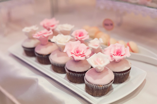 White plate on the table with cupcakes ornate with sweet roses; cookies on the background