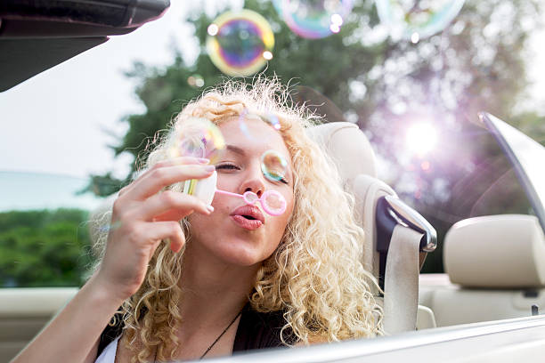 istock Young woman blowing soap bubbles in a cabrio. 587814072